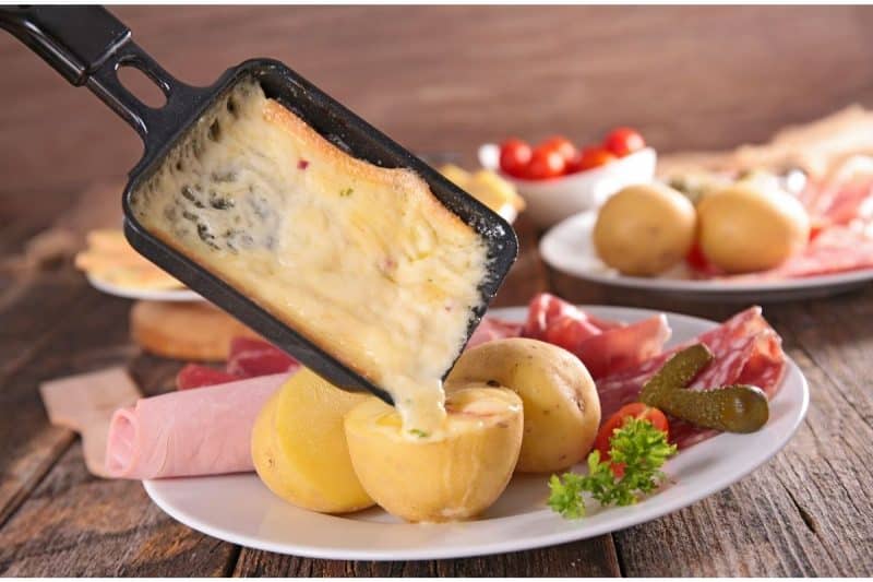 Melted raclette cheese being poured over boiled potatoes